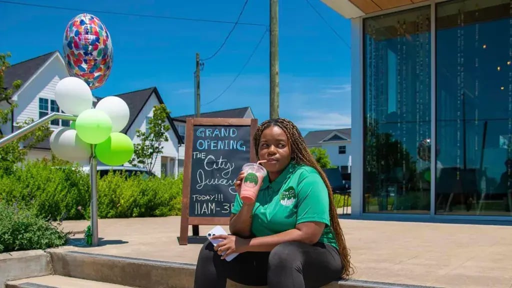Kayla Hall-Ransom, founder of The City Juicery in Nashville. | Woman sitting on stairs outside at a juicery grand opening, drinking a smoothie.