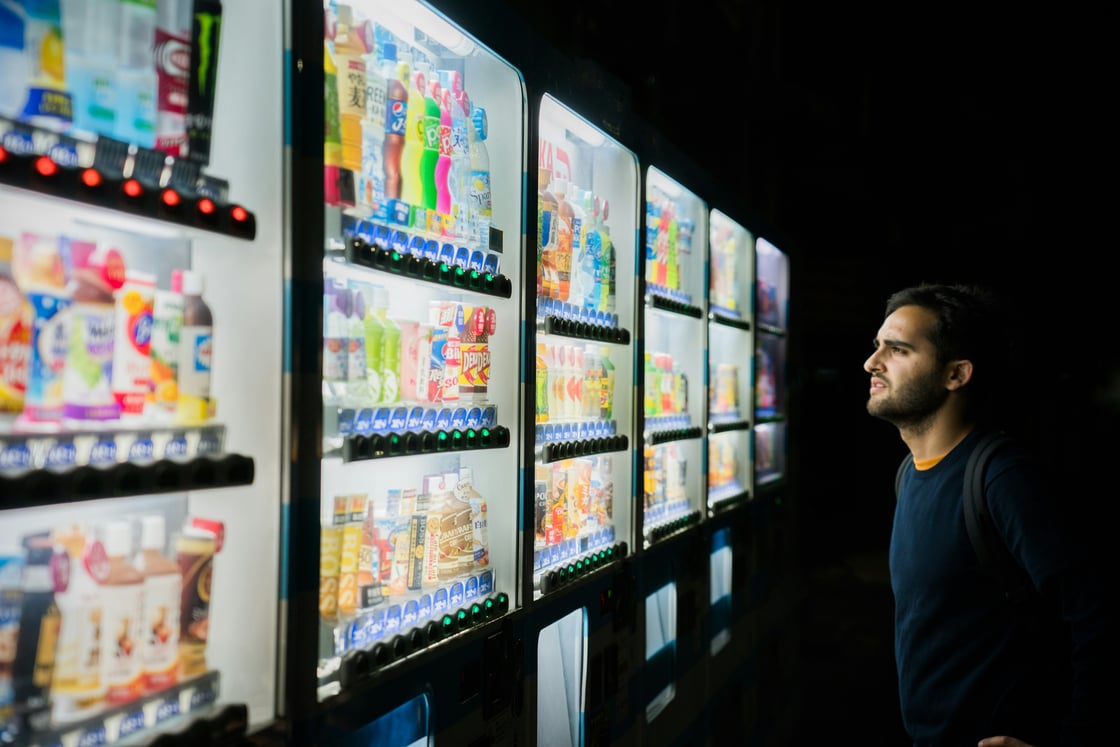 Image of a man standing in front of several vending machines, trying to make a decision.
